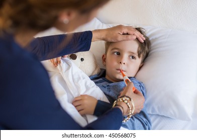 Sick boy with thermometer laying in bed and mother hand taking temperature. Mother checking temperature of her sick son who has thermometer in his mouth. Sick child with fever and illness in bed. - Shutterstock ID 450568075