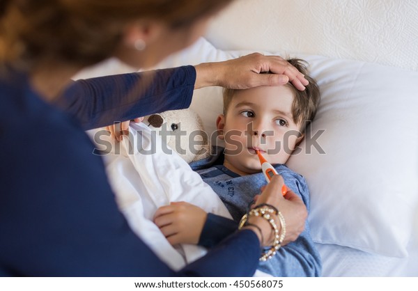 Sick boy with thermometer laying in bed and mother\
hand taking temperature. Mother checking temperature of her sick\
son who has thermometer in his mouth. Sick child with fever and\
illness in bed.