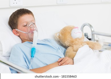 Sick boy wearing oxygen mask sleeping beside teddy bear in hospital bed - Powered by Shutterstock