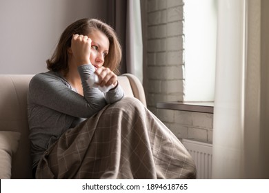 Sick brunette woman with headache having cold and flu sneezing sitting on the couch in the living room near window 