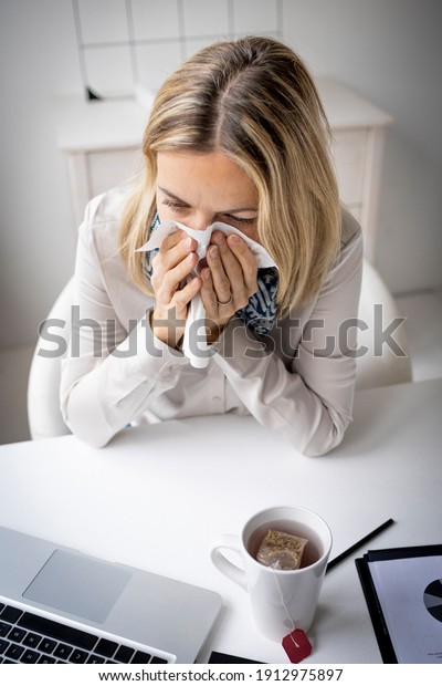 Sick business woman in office feeling\
unwell sitting in front of her laptop blowing her nose, stressed\
femal employee have anxiety attack at\
workplace