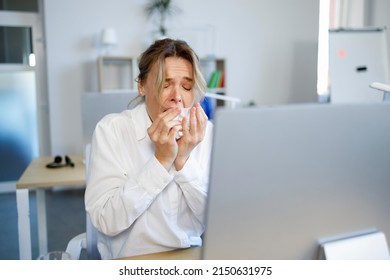 Sick business woman sneezes while sitting at the workplace in the office. Portrait of female white collar worker who suffers from allergies - Powered by Shutterstock