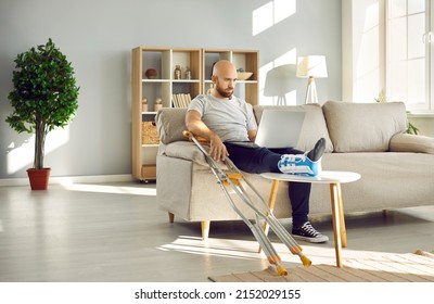 Sick businessman with broken leg in bandage sit on sofa at home work on laptop online. Unhealthy man with foot injury in splint use computer during leave. Trauma and rehabilitation. Medicine concept. - Powered by Shutterstock