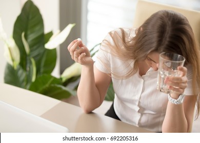 Sick Businesswoman Holding Glass Of Water And Medical Pill At Workplace, Suffering From Migraine Headache, Feeling Bad, Taking Medicine At Work, Depressed Woman Addicted To Antidepressant Tablets