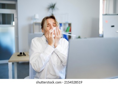 Sick businesswoman sneezing in a tissue while working in the office - Powered by Shutterstock