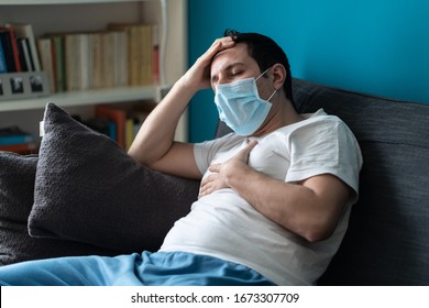 A Sick Caucasian Man Wearing Face Mask Feeling Sick Headache And Cough Because Of Coronavirus Covid-19 On The Sofa In Quarantine