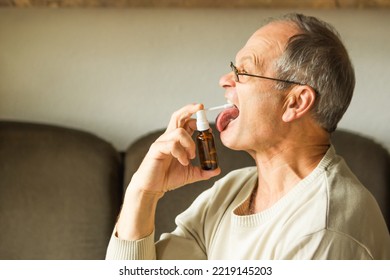 Sick Caucasian Senior Man With Open Mouth And Long Tongue Using A Throat Spray Against A Dry Cough. Health Care Concept.