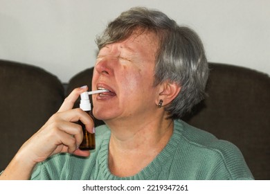 Sick Caucasian Senior Woman With Open Mouth Using A Throat Spray Against A Dry Cough. Health Care Concept.