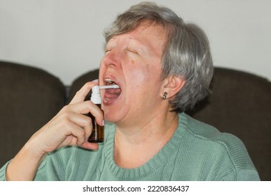 Sick Caucasian Senior Woman With Open Mouth Using A Throat Spray Against A Dry Cough. Health Care Concept.