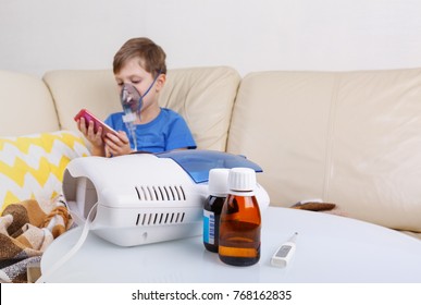 Sick Chid With Pediatric Nebulizer Entertaining Himself By Playing Games On Mobile Phone, Medicines And Thermometer In The Foreground. Little Kid With Asthma Or Bronchitis Has Trouble Breathing.