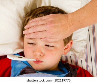 Sick Child Boy Being Checked For Fever And Illness While Resting In Bed