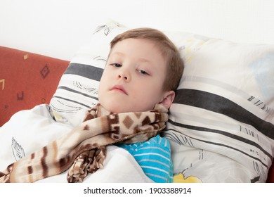 sick child boy in a blue sweater with a scarf in bed waiting for recovery