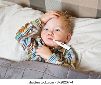 Sick Child Boy Lying In Bed With A Thermometer In Mouth And Touch His Forehead