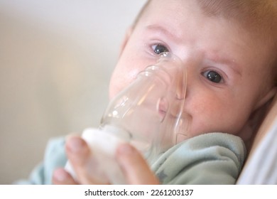A sick child breathes with a nebulizer mask with a steam inhaler due to a respiratory disease. A mother holding an inhaler in her hands - Shutterstock ID 2261203137