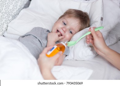 Sick Child Concept. Mother Giving Her 2 Years Old Baby Boy Medicine, Cough Syrup On A Spoon.