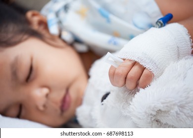 Sick Child Girl's Hand With Saline Intravenous (iv) Drip Hugging Her Doll While Sleeping In The Hospital