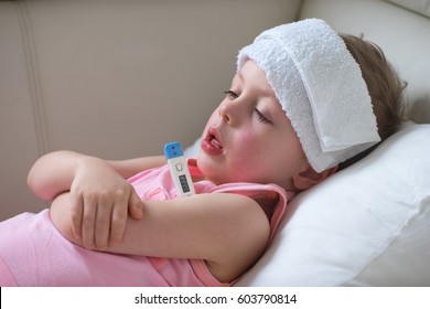  Sick Child With High Fever Laying In Bed And  Holding Thermometer.  Compress On Forehead.