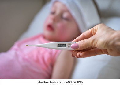  Sick Child With High Fever Laying In Bed And  Holding Thermometer.  Compress On Forehead.