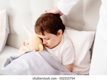 Sick child hugging a teddy bear in bed.