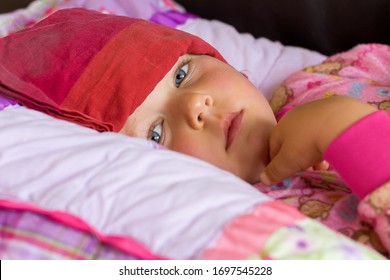 Sick Child Looks Miserably At Camera While Resting With A Cold Compress On Forehead