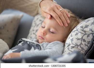 Sick child, toddler boy lying on the couch in living room with a fever, mom cheching his temperature, resting at home - Powered by Shutterstock