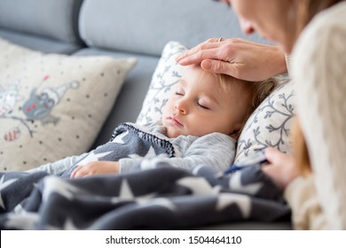 Sick Child, Toddler Boy Lying On The Couch In Living Room With A Fever, Mom Cheching His Temperature, Resting At Home