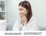 Sick, coronavirus or covid, tired asian young woman have a fever, flu and hand in use tissues paper sneezing nose, runny while sitting on sofa, couch at home. Health care with disease, pandemic virus