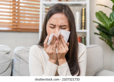 Sick, Coronavirus covid-19 asian young woman, girl headache under blanket have a fever, flu and use tissues paper sneezing nose, runny sitting on sofa bed at home. Health care on virus person. - Shutterstock ID 2107321733
