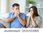 Sick couple at home blowing on tissue looking each other siting on a couch