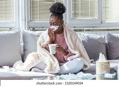 Sick day at home. African American woman has runny nose and common cold. Cough. Closeup Of Beautiful Young Woman Caught Cold Or Flu Illness. Portrait Of Unhealthy Girl Drinking Tea.