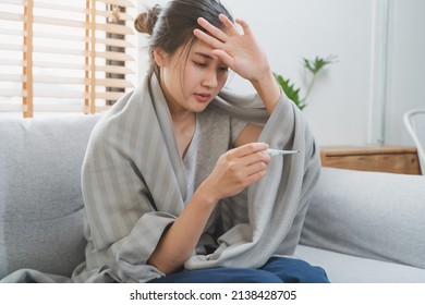 Sick day at home in winter season. Young asian woman have a fever checking thermometer and measure body temperature. - Shutterstock ID 2138428705