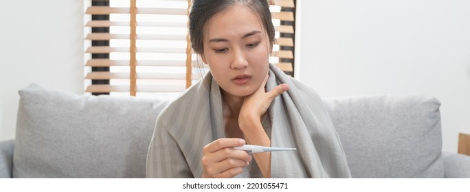 Sick Day At Home In Winter Season. Young Asian Woman Have A Fever Checking Thermometer And Measure Body Temperature.