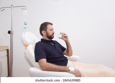 Sick, dehydrated or hangover patient man receiving vitamin IV infusion drip and drinking glass of water in hospital or beauty salon. Healthcare and medicine concept