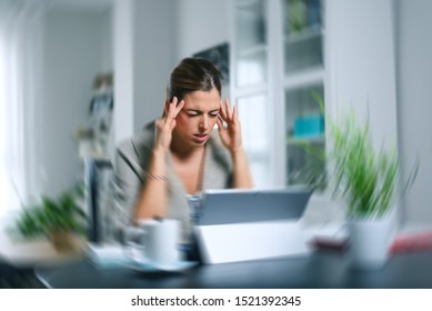 Sick dizzy young woman suffering headache while working on her laptop at home. Covid-19 woman on quarentine doing tele work and suffering symptoms.