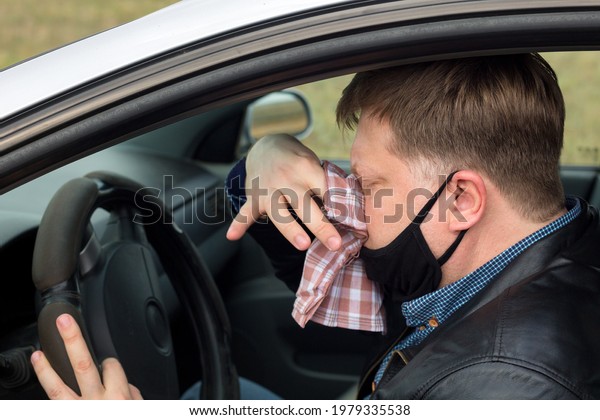 A sick driver in the car wipes his snot\
with a handkerchief.