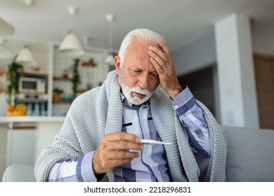 Sick elderly man checking his temperature suffering from seasonal flu or cold lying on sofa caughing suffering from seasonal flu or cold. . Ill senior feel unhealthy with influenza at home - Powered by Shutterstock