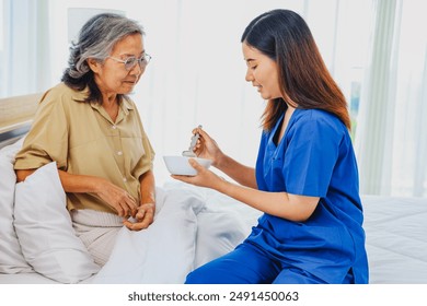 Sick elderly woman is closely cared for female nurse who is taking care of her. She slowly scoops porridge into her mouth nutritious cooked breakfast. Help her recover from her illness in bed at home. - Powered by Shutterstock