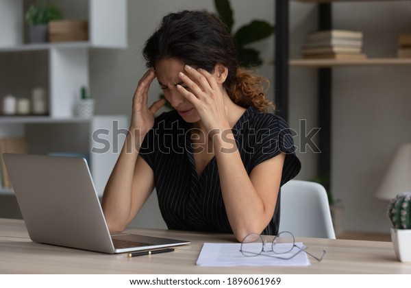 Sick exhausted Caucasian female work on laptop\
struggle with migraine or headache. Tired unwell young woman take\
off glasses overwhelmed with computer job suffer from blurry vision\
or dizziness.