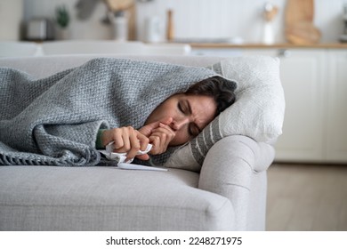 Sick exhausted woman lying on couch wrapped in blanket and coughs after being infected with dangerous flu or viral infection. Suffering unhappy girl with handkerchief and thermometer needs help doctor