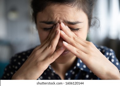 Sick frustrated sad young indian woman in pain cope with headache, eye strain emotional mental stress cry feel anxiety pressure panic attack touching nose bridge, face close up view, migraine concept