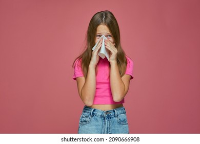 Sick girl child cry, blowing runny nose, sneezing in tissue, suffer seasonal allergy or flu symptoms on pink background