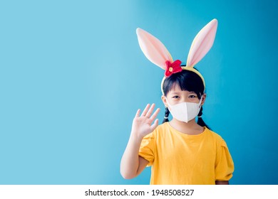 Sick Girl Child In Medical Mask Isolated On Blue Background.Coronavirus Covid19.Online Education Home.Asian Kid Girl Wearing Face Mask In Easter Holiday.hello Waving Hands.Homeschool Kid With Mask.