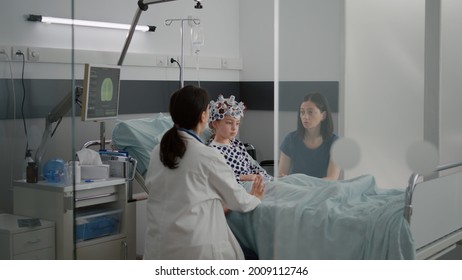 Sick Girl Child Patient Wearing Eeg Headset With Sensors While Pediatrician Doctor Monitoring Brain Tomography Evolution Checking Expertise On Monitor. Kid Resting In Bed In Hospital Ward