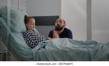 Sick Girl Daughter Sleeping After Surgery Recovery While Worried Father Praying For Kid Healthcare During Medical Consultation In Hospital Ward. Child Wearing Oxygen Nasal Tube Resting In Bed