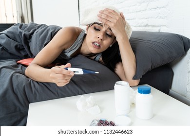 Sick Hispanic Woman In Bed Calling In Sick Day Off From Work Thermometer To Check Temperature For Fever And Vitamins Hot Water Bottle And Tissues In Cold And Flu Concept