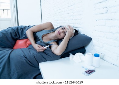 Sick Hispanic Woman In Bed Calling In Sick Day Off From Work Thermometer To Check Temperature For Fever And Vitamins Hot Water Bottle And Tissues In Cold And Flu Concept