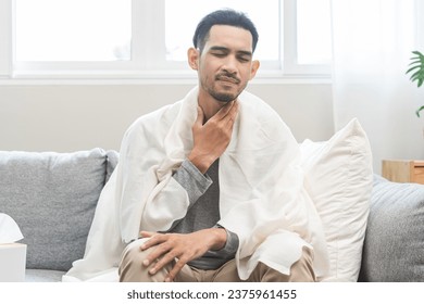 Sick, hurt asian young man sore throat pain, have a fever, flu touching massage neck. Painful male cold and infection while sitting sad on couch at home. Healthcare medical of influenza virus seasonal - Powered by Shutterstock