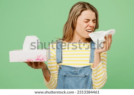 Sick ill allergic sad woman has watery eyes runny stuffy sore nose suffering from allergy trigger symptoms hay fever holding paper napkin handkerchief sneeze isolated on plain green background studio