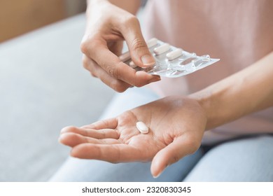 Sick ill asian young woman, girl hand taking tablet pill capsule out from blister pack, painkiller medicine from stomach pain, head ache, pain for treatment, take drug or vitamin at home, health care. - Powered by Shutterstock