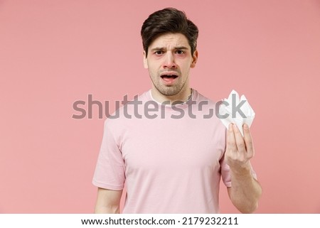Sick ill tired crying allergic man has watery red eyes runny nose suffer from allergy hay fever hold paper napkin isolated on pastel pink color background studio. Spring rhinitis reaction on trigger